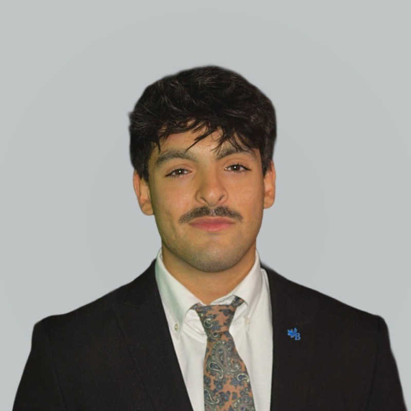Headshot of Myles Manoli in a dark suit and paisley tie